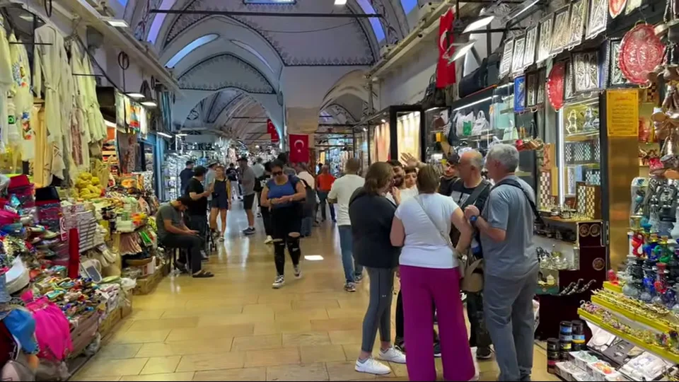Shoppers pause beside bag and souvenir stalls in the Grand Bazaar